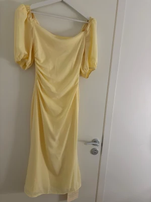 Adoore klänning  - Supersöt långklänning i ljusgul färg med puffiga korta ärmar och lätt rynkning i sidan. Klänningen har en mjuk, följsam passform och en elegant, enkel design som känns både trendig och romantisk. Helt ny 