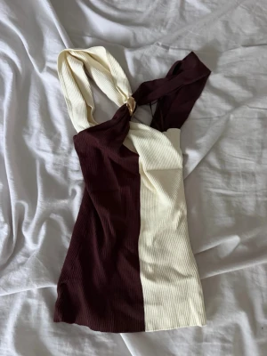 Tvåfärgad ribbad oneshoulder topp - Säljer en snygg ribbad topp med oneshoulder-design i mörkbrunt och beige. Toppen har en unik twistad axelband och är croppad, perfekt för att sticka ut i mängden.