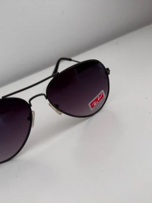 Svarta Ray-Ban inspirerade aviator solglasögon - Snygga svarta aviator solglasögon från Ray-Ban med tunna metallbågar och mörka tonade glas. Klassisk pilotmodell som ger en cool och tidlös look. Perfekta för att lyfta vilken outfit som helst.