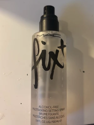 MAC Fix+ Face Mist 100 ml - MAC Fix+ är en alkoholfri face mist i en genomskinlig plastflaska med svart spraymunstycke. Perfekt för att fräscha upp huden och fixera makeup. Flaskan rymmer 100 ml och har en stilren design med svart text.