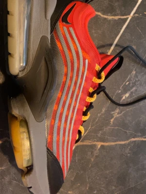 Nike röda sneakers med luftdämpning - Snygga röda Nike sneakers  kunde inte lägga in det bara  luftdämpad sula och svarta samt grå detaljer. Skon har flera reflekterande ränder på sidan, gula skosnören och svart logga på ovandelen. Ovandelen är i mesh och syntetmaterial för bra andningsförmåga.