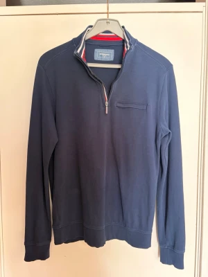 Marinblå halvzip tröja Dressmann - Snygg marinblå långärmad tröja från Dressmann med halvzip och ståkrage. Tröjan har en diskret bröstficka och ribbade muddar vid ärmslut och nederkant. Perfekt för en avslappnad men stilren look.