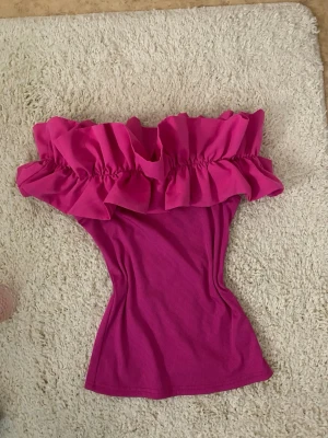 Rosa offshoulder topp med volang - Trendig rosa offshoulder topp med bred volang runt axlarna. Aldrig använd💗