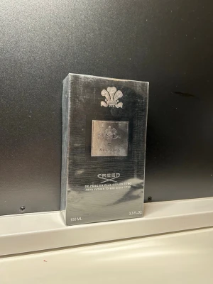 Creed Aventus Eau de Parfum 100 ml - Lyxig parfym från Creed, Aventus, i en elegant svart och silverfärgad förpackning. Flaskan rymmer 100 ml och har exklusiv design med Creed-logga och metallisk etikett. Doften är känd för sina fruktiga och träiga noter, perfekt för dig som vill sticka ut.