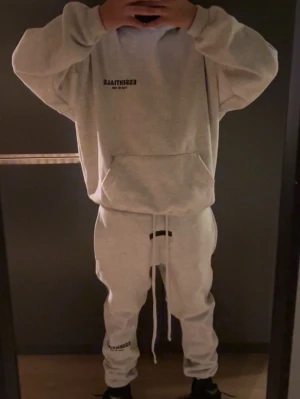 Grå/beige Essentials loungewear set - Kan köpa endast hoodie eller byxor. !!!!Mysigt grått loungewear set från Essentials med hoodie och matchande byxor. Hoodien har magficka och tryck på bröstet, byxorna har dragsko i midjan och tryck på benet. Perfekt för chill dagar hemma eller när du vill vara bekväm.