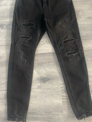 Svarta slitna skinny jeans - Säljer ett par svarta skinny jeans med flera slitningar och hål på både fram- och baksida. Jeansen har en smal passform och råa kanter vid bensluten. Perfekta för en edgy och trendig look. 38 storlek, 30 längd 