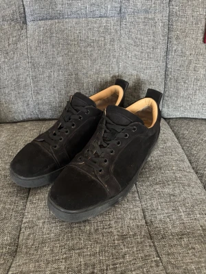  Christian Louboutin  - Snygga svarta sneakers i mocka med svart sula och kontrasterande röd undersida. Skorna har klassisk låg profil, svarta skosnören och beige innerfoder. Perfekta för en clean och stilren look. Priset kan diskuteras men måste ha en anledning för att kunna pruta
