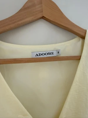 Ljusgul omlottklänning från Adoore - Supersöt ljusgul omlottklänning från Adoore med puffiga långärmar och v-ringning. Klänningen har broderade detaljer och en öppen midja som ger en unik look. Perfekt för sommarens alla tillfällen! Banden kan man knyta på lite olika sätt för att få den att passa så som man vill! Den är endast använd 1 gång men tyvärr har den varit lång på mig så den har fått smuts längst ner vid kanten som jag inte lyckats få bort i tvätten. Går säkert bort med starkt medel. Inget som syns när man har på sig den❤️