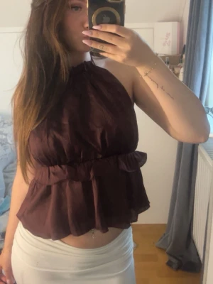 Vinröd haltetnecktopp - Snygg visnröd topp med volangdetaljer och öppen rygg. Toppen har halterneck och en luftig, flowy passform som ger en trendig look. Perfekt att styla med både jeans och kjol. Använd en gång ute och testad  några gånger.