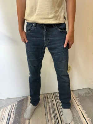 Tiger of Sweden Mörkblå slim fit jeans W33 L32 går bra att pruta - Säljer ett par mörkblå slim fit jeans med klassisk femficksdesign och snygga sömdetaljer över låren. Jeansen har normal midja och raka ben, perfekta till en avslappnad stil. Materialet är mjukt denim som ger en bekväm känsla hela dagen.