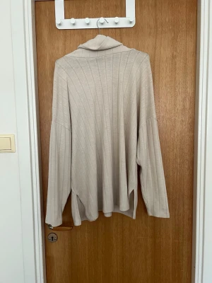 Beige stickad polotröja från Stories - Säljer en oversized beige stickad polotröja från Stories. Tröjan har långa ärmar, ribbade detaljer och en hög polokrage. Perfekt för lager på lager och chill stil. Materialet känns mjukt och följsamt.🤍 
