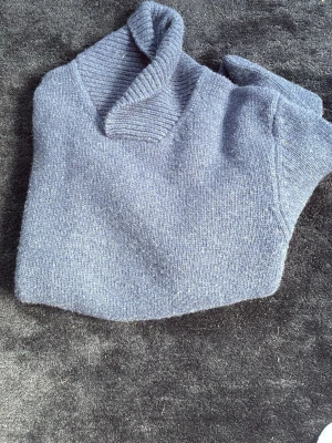 Grå stickad tröja med krage - Mysig grå stickad tröja med bred ribbad krage och långa ärmar. Tröjan har ribbade muddar vid ärmslut och nederkant. Perfekt för kyliga dagar och enkel att matcha med olika outfits.