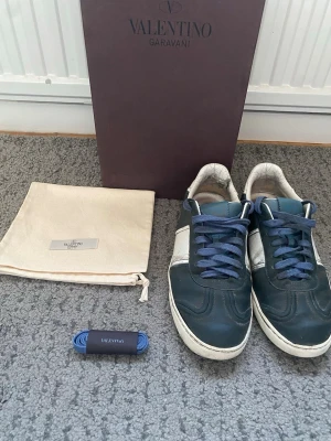 Valentino Garavani flycrews blå/vit - Snygga sneakers från Valentino Garavani i mörkblått och vitt läder med blå skosnören. Klassisk låg modell och extra blåa skosnören samt originalkartong. Perfekta för dig som gillar exklusiva märken och stilren design. Dom har inga sulor.