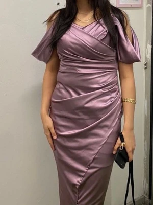 Lila omlottklänning i satin - Snygg lila långklänning i glansigt satinmaterial med omlottdetalj och draperingar. Klänningen har offshoulder-ärmar och en figurnära passform som framhäver siluetten. Perfekt för dig som vill sticka ut med en elegant look.