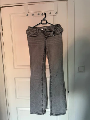 Grå bootcut jeans från Gina tricot  - Säljer ett par grå bootcut jeans från Gina tricot. Jeansen har klassisk femficksmodell, bälteshällor och knappgylf. Materialet är mjukt denim med en lätt tvättad look. Perfekta för dig som gillar en avslappnad men ändå trendig stil. De har använts men de är i bra skick. 