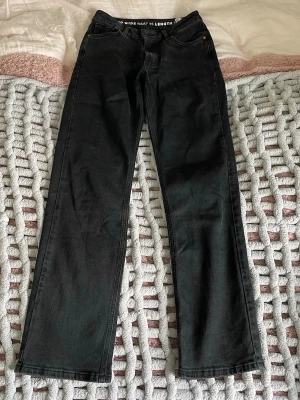 Svarta raka jeans  - Snygga svarta jeans med rak passform och mellanhög midja. Jeansen har klassiska fem fickor, bälteshällor och knappgylf. W25 L32 