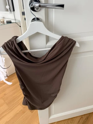 Brun axelbandslös tubtopp - Snygg brun axelbandslös tubtopp med draperad ringning. Perfekt för dig som vill ha en enkel men trendig topp till sommaren. Mjuk och stretchig känsla i materialet.