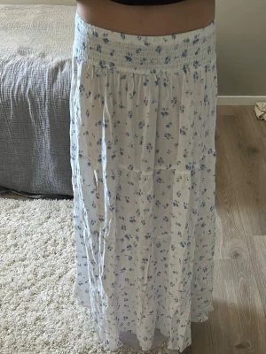 Vit långkjol med blå blommor och slits - Säljer en luftig och flowy långkjol i vitt med små blå blommor, och en snygg slits på sidan som ger extra edge. 