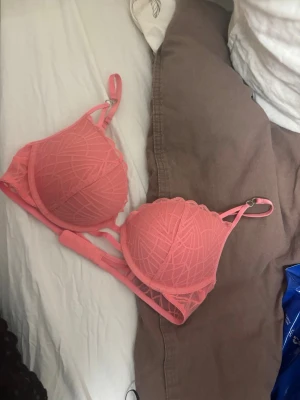 Rosa push-up bh från Triumph - Säljer en snygg rosa push-up bh från Triumph med vadderade kupor och justerbara axelband. Bh:n har ett dekorativt mönster i spets och ger bra stöd och form. Perfekt för dig som vill ha något både bekvämt och stilrent.