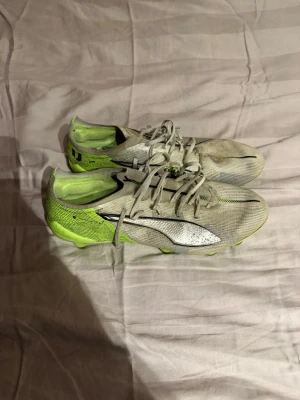 Vita och neongröna Puma fotbollsskor - Säljer ett par snabba fotbollsskor från Puma i vitt och neongrönt med svarta detaljer. Skorna har klassisk snörning, låg profil och mönstrad ovandel för bra bollkontroll. Perfekta för dig som vill sticka ut på planen och få grymt grepp på gräs.