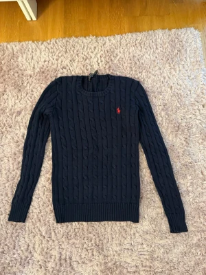 Mörkblå kabelstickad tröja - Mörkblå kabelstickad tröja med rund halsringning och långa ärmar. Äkta Ralph Lauren. Skickar snabbt🥰🥰