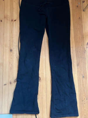 Svarta bootcut mjukisbyxor lowwaist - Säljer ett par svarta mjukisbyxor med bootcut passform och bred resår i midjan. Byxorna har dragsko för justerbar midja och är gjorda i ett mjukt, stretchigt material som är perfekt för chill dagar. Klassisk och enkel design som funkar till det mesta.