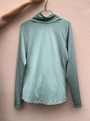 Ljusgrön polotopp med lång ärm - Säljer en stilren ljusgrön polotopp med långa ärmar. Toppen har en mjuk, slät yta och en hög krage som ger en clean look. Perfekt att matcha med jeans eller kjol för en trendig outfit.