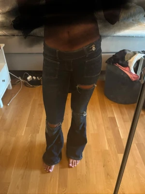 Mörkblå bootcut jeans med slitningar - Säljer ett par mörkblå bootcut jeans med slitna detaljer vid knäna. Jeansen har hög midja, framfickor och markerade sömmar. Perfekta för en trendig och avslappnad stil. Materialet är klassisk denim med lite stretch.