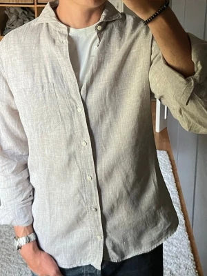 Eton linneskjorta i beige - stl 42 (L) - Eton linneskjorta i beige, storlek 42 (L). Slim fit i 100% linne. Tunt och luftigt tyg. Personen på bilden är 189cm, väger 78kg.  Använd men i mycket fint skick, inga hål eller fläckar.  Rök- och djurfritt hem. Skriv gärna om du vill ha fler bilder eller undrar något!