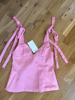 Rosa populär satintopp   - Supersöt rosa topp med knytband på axlarna och figurnära passform. Toppen har en lätt glansig yta och markerade kupor för en snygg siluett.  Den är helt ny !!💕