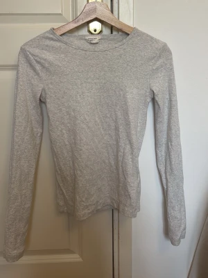 Ljusgrå långärmad topp - En enkel och stilren ljusgrå långärmad topp med rund hals. Tillverkad i mjukt bomullsmaterial som känns skönt mot huden. Perfekt att matcha med jeans eller kjol för en clean look.
