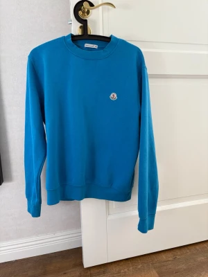 Blå sweatshirt från Moncler - Snygg blå sweatshirt från Moncler med rund halsringning och diskret Moncler-logga på bröstet. Tröjan har en klassisk passform, ribbade muddar vid ärmslut och nederkant samt är tillverkad i mjukt material. Perfekt för en avslappnad och stilren look.