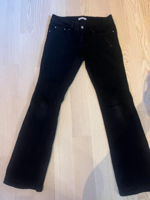 Svarta bootcut jeans - Säljer ett par svarta bootcut jeans med klassisk femficksmodell och silverfärgade nitar. Jeansen har normal/låg midja och bälteshällor. Perfekta för dig som gillar en tidlös och enkel stil.