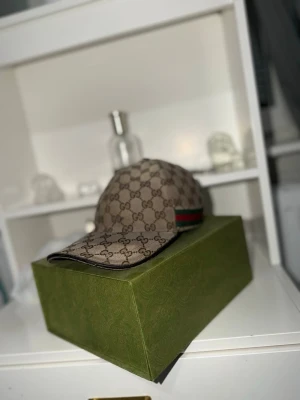 Beige Gucci Keps - Säljer en fantastisk och exklusiv gucci keps som inte säljs längre. Den är väl omhändertagen och i jättebra skick. Box och allt följer med. Storlek S
