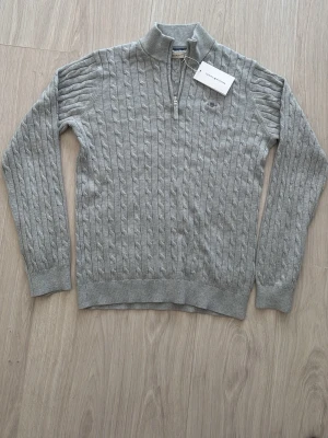 Gant stickad tröja  - Snygg ljusgrå kabelstickad ganttröja som jag köpte från kidsbrandstore för cirka 1200kr fast på rea som jag nu säljer. Den har ej varit använd och priset kan diskuteras! 