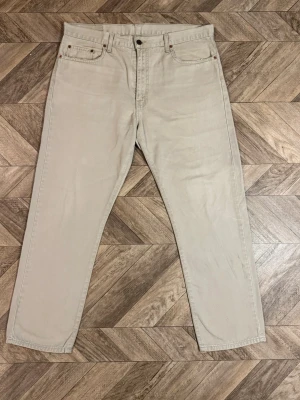 Beige Levi's 615 - Snygga beige jeans från Levi's med rak passform och klassiska fem fickor. Jeansen har en enkel design med knappgylf och Levi's ikoniska läderpatch bak i midjan. Perfekta för en clean och avslappnad stil.Längd 101cm Bredd 48cm
