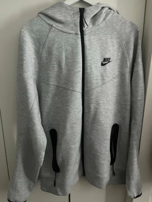 Nike Tech Hoodie - Nike Tech Hoodie – Strl L  Säljer en grå Nike Tech Fleece hoodie i storlek L. Bekväm passform och perfekt till vardag eller gym. Fint skick utan större anmärkningar. Skickas snabbt eller möts upp vid affär.