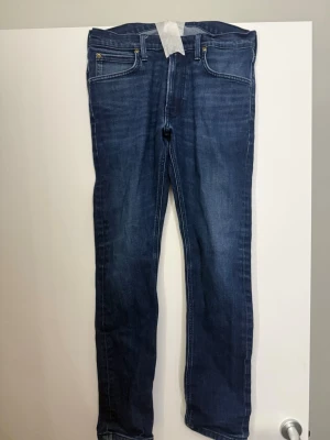 Mörkblå slim fit jeans - Säljer ett par mörkblå slim fit jeans med klassisk femficksdesign och kontrastsömmar. Jeansen har raka ben och är tillverkade i ett stretchigt denimtyg för extra komfort. Passar perfekt till en avslappnad och trendig stil.