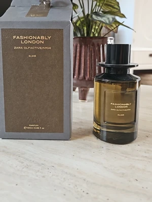 Fashionably London Elixir parfym 100ml - Parfymen Fashionably London Elixir från Zara Olfactive/No4 kommer i en elegant, cylindrisk glasflaska med svart lock och guldtext. Flaskan rymmer 100 ml och har en stilren, modern design med tillhörande mörkgrå kartong. Köpte för ett par månader sedan. Men knappt använd.