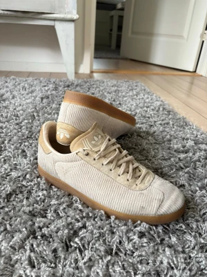 Beige sneakers Adidas Gazelle - Snygga sneakers från Adidas i beige manchestertyg med klassiska tre ränder på sidan och gummisula i brunt. Skorna är inte använda mkt men finns lite små smuts som man ser på bilden! Annars väldigt bra skick! Väldigt unik sko😁