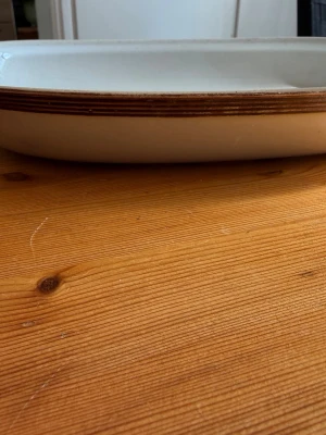 Vitt rektangulärt porslinsfat - Ett vitt rektangulärt fat i porslin med bruna ränder längs kanten. Perfekt för servering eller matlagning. Enkel och klassisk design som funkar i alla kök.