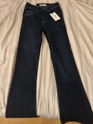 Bootcut jeans mörkblå XS - Mörkblå bootcut jeans i modellen Blake med kontrastsömmar och klassisk femficksdesign. Jeansen har hög midja och är tillverkade i denim med stretch för extra komfort. Snygg passform som ger en tidlös look.