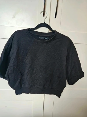 Svart croppad t-shirt från 157 - croppad tröja från 157  Säljer en croppad tröja från 157 i storlek S. Tröjan har korta ärmar, rund hals och bred ribbad kant nedtill. Tillverkad i mjuk bomull, perfekt för chill dagar. Enkel och stilren design som är lätt att matcha med jeans eller shorts.  Kan även hämtas I Partille  E1