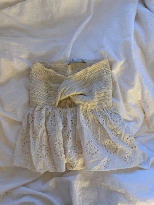 Söt off shoulder topp  - Superfin off shoulder topp i ljusbeige med virkad överdel och broderad, luftig nederdel. Toppen har twistad detalj framtill och är perfekt för varma dagar. Materialet är bomull och toppen har en romantisk vibe.