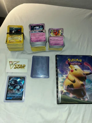 Pokemon bulk 500 kort +med pärm och toploaders - Säljer en stor samling Pokémonkort med flera olika kortlekar, en VSTAR-markör, kortfodral, ett specialkort i plastficka och en Pokémon-pärm med Pikachu på omslaget. Perfekt för samlare eller dig som vill börja spela Pokémon Trading Card Game.     Sakerna du får:   En lumineon v kort i sleeve och toploader, sleeves och toploaders , en pärm som är four pocket och till sist , 500 kort + bulk kort från 2018-2026