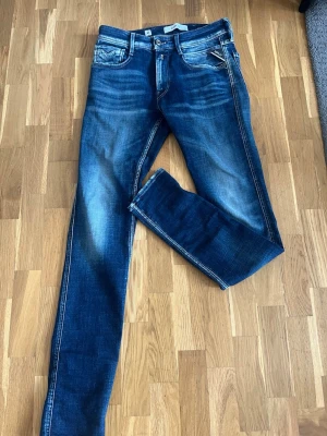 Blå slim fit jeans från Replay - Snygga blå slim fit jeans från Replay, modell Anbass. Jeansen har klassisk femficksdesign, slitningar och snygg tvätt med ljusare partier framtill och på låren. Perfekta för dig som gillar en modern och avslappnad stil.