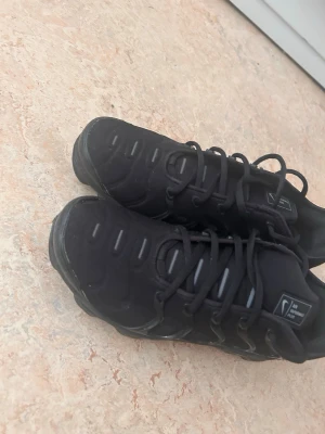 Svarta sneakers med sportig design - Svarta sneakers med sportig look och snörning. Skorna har en låg siluett och detaljer i svart och grått. Ovandelen verkar vara i syntetmaterial och mesh för extra komfort. Sulan är robust och ger bra grepp. Perfekta för en aktiv vardag.
