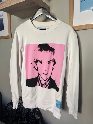 Vit CK sweatshirt med popkonst-tryck - Snygg vit sweatshirt från CK med ett stort Andy Warhol tryck i rosa och svart på framsidan. Tröjan har rund halsringning, långa ärmar och ribbade muddar. Tillverkad i mjukt bomullsmaterial för en bekväm känsla.