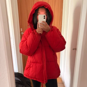 Röd pufferjacka från H&M med huva - Säljer en röd pufferjacka från H&M i storlek M. Jackan har en stor huva, dragkedja framtill och en klassisk quiltad design. Perfekt för kalla vinterdagar och riktigt skön att bära. Materialet är syntetiskt och jackan är vadderad för extra värme.