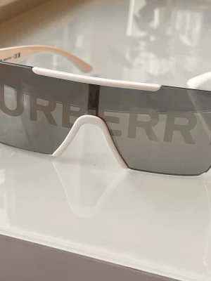 Burberry solglasögon - Säljer ett par riktigt snygga Burberry solglasögon med Burberry-loggan tryckt över hela framsidan. 